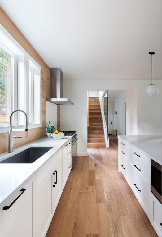 Parallel kitchen layout with white cabinets and wood flooring