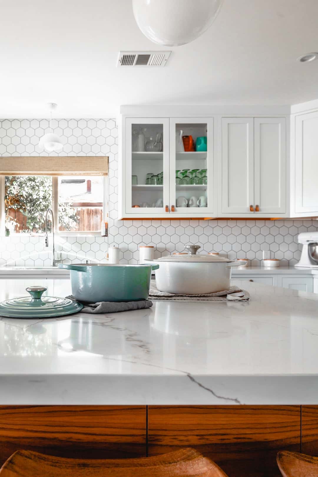 Airy straight kitchen design with marble island, hex tile backsplash, and open cabinetry.