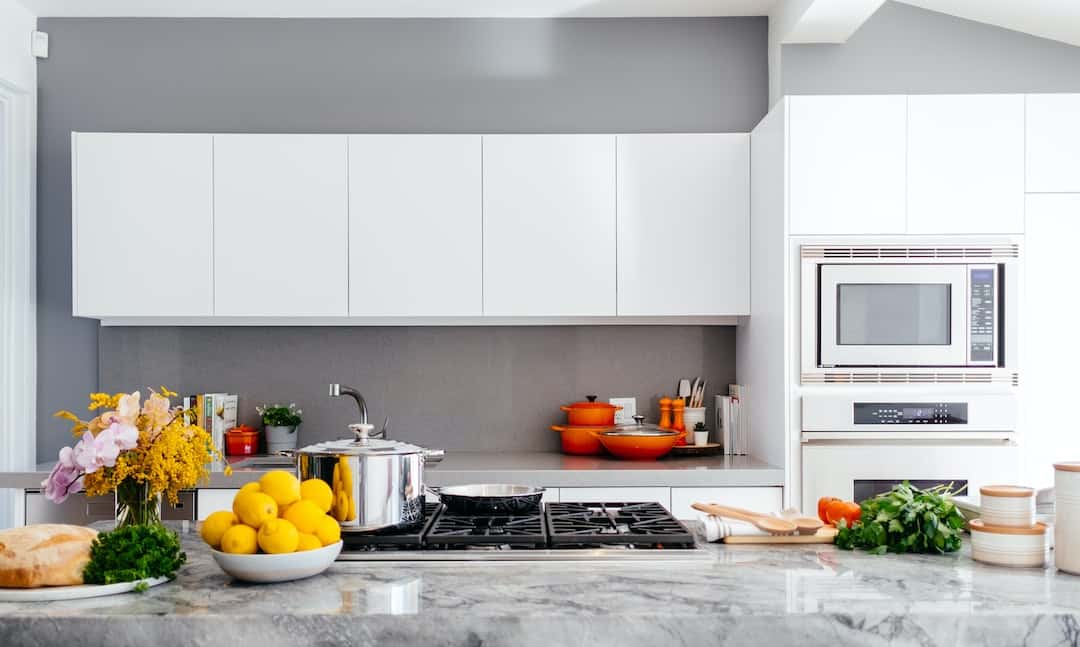 Bright straight kitchen design with white cabinets, marble counter, and bold orange accents.