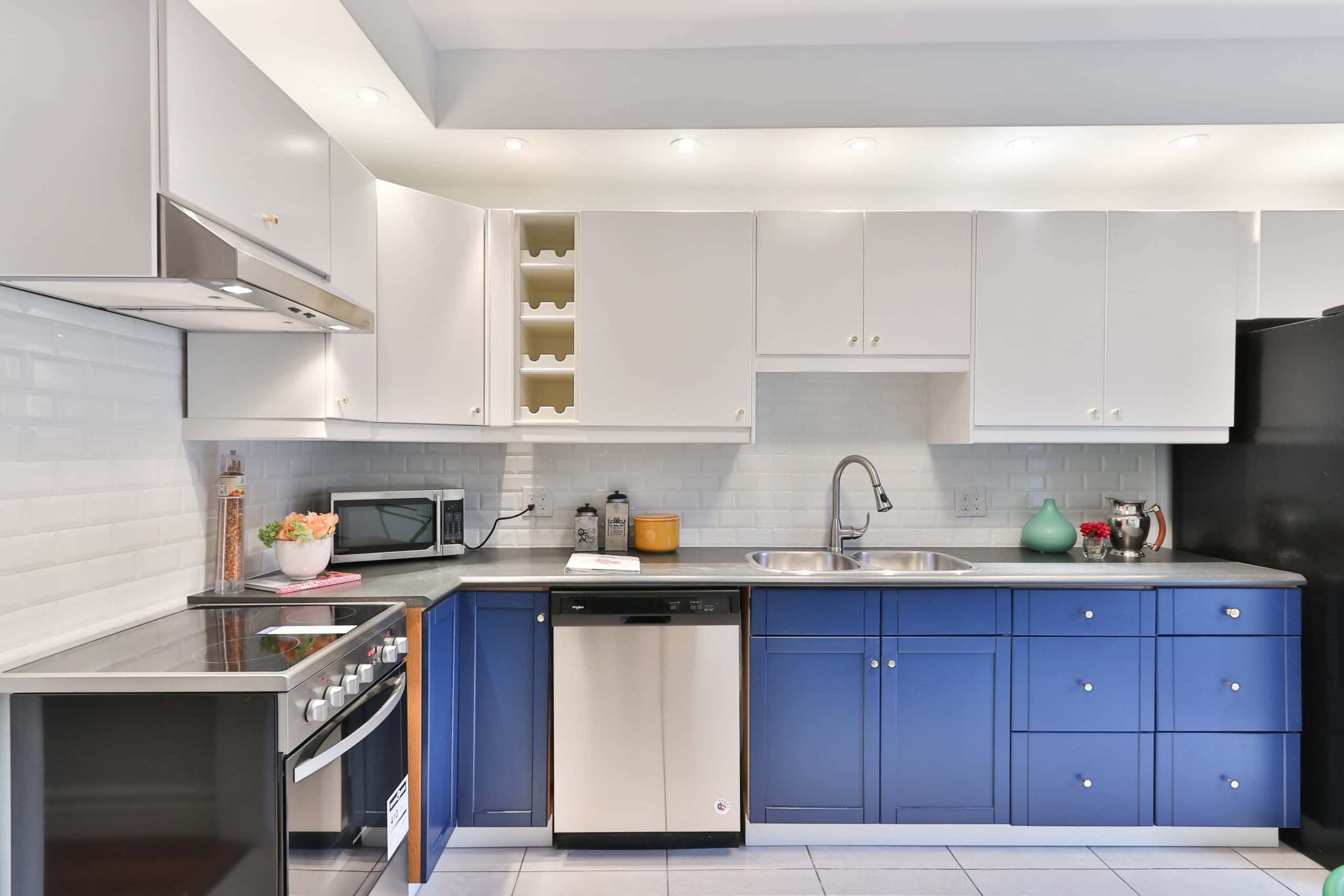 Clean industrial kitchen with blue lower cabinets white uppers and subway tile walls