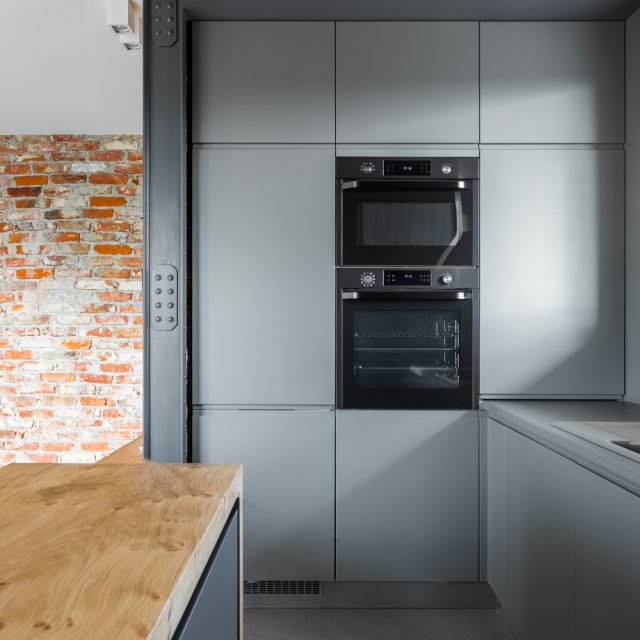 Industrial loft kitchen design with modular gray cabinets and exposed brick wall