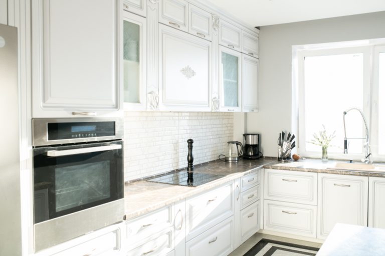 Bright modular kitchen with loft featuring white cabinets, built-in oven, and marble countertop