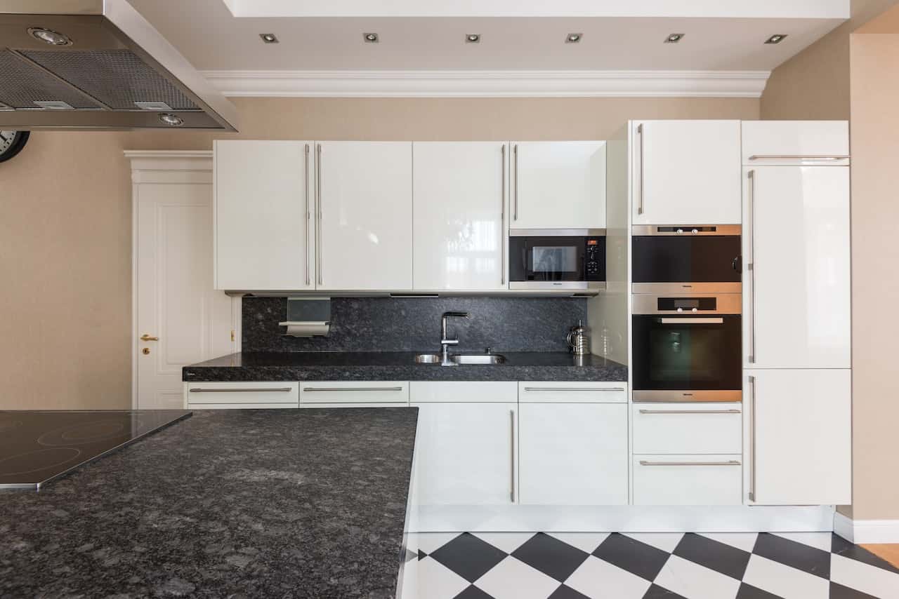 Glossy kitchen door designs with sleek white cabinets and black stone countertop