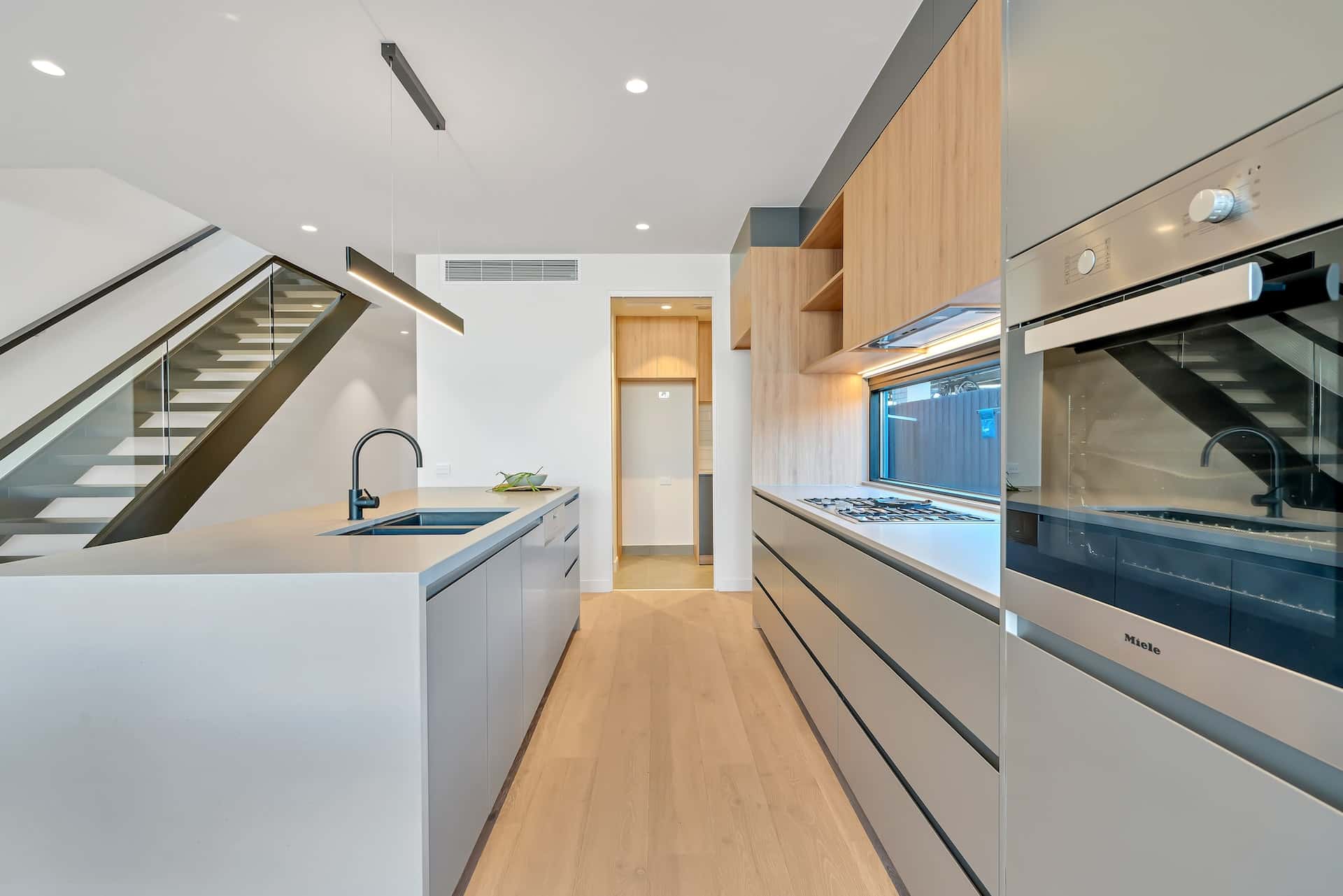 Minimalist kitchen entrance design featuring white countertops and staircase view