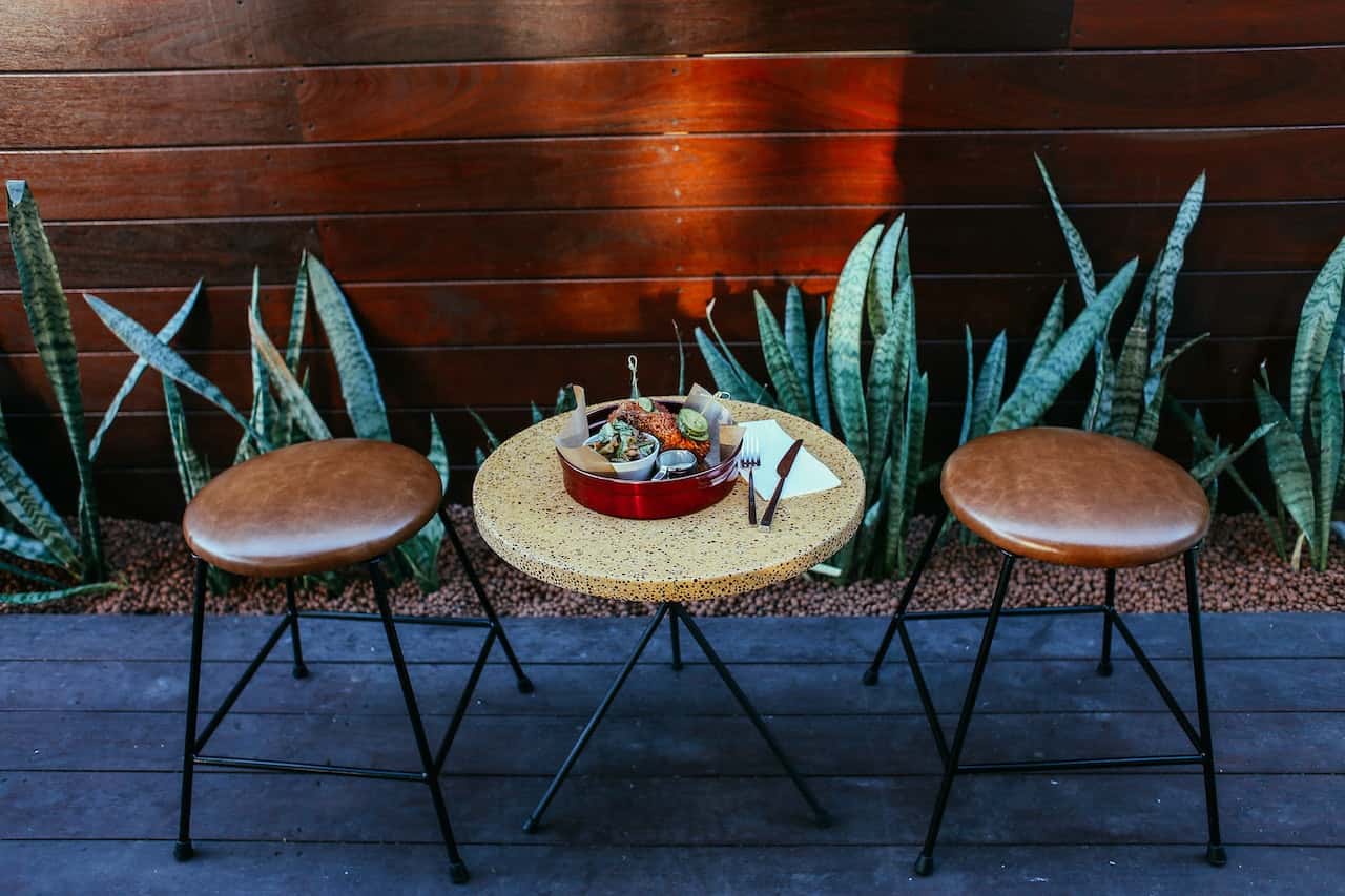 Cozy sitout design with round table, leather stools, and a stylish wooden backdrop