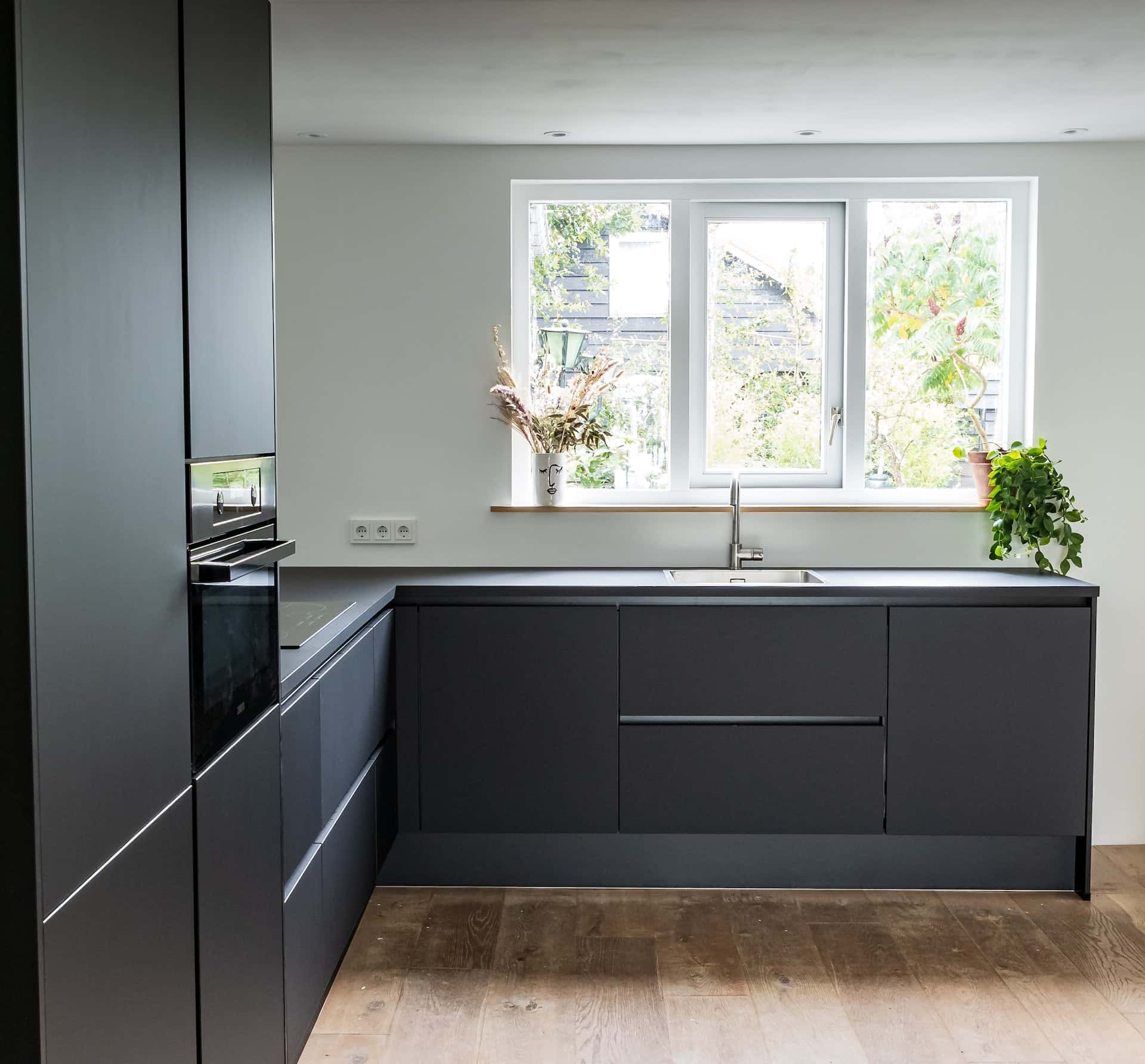 Matte gola profile handles in a dark modular kitchen with wooden flooring