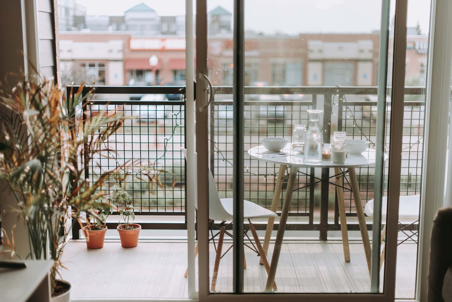 Compact closed balcony ideas with glass doors, table setup, and potted plants