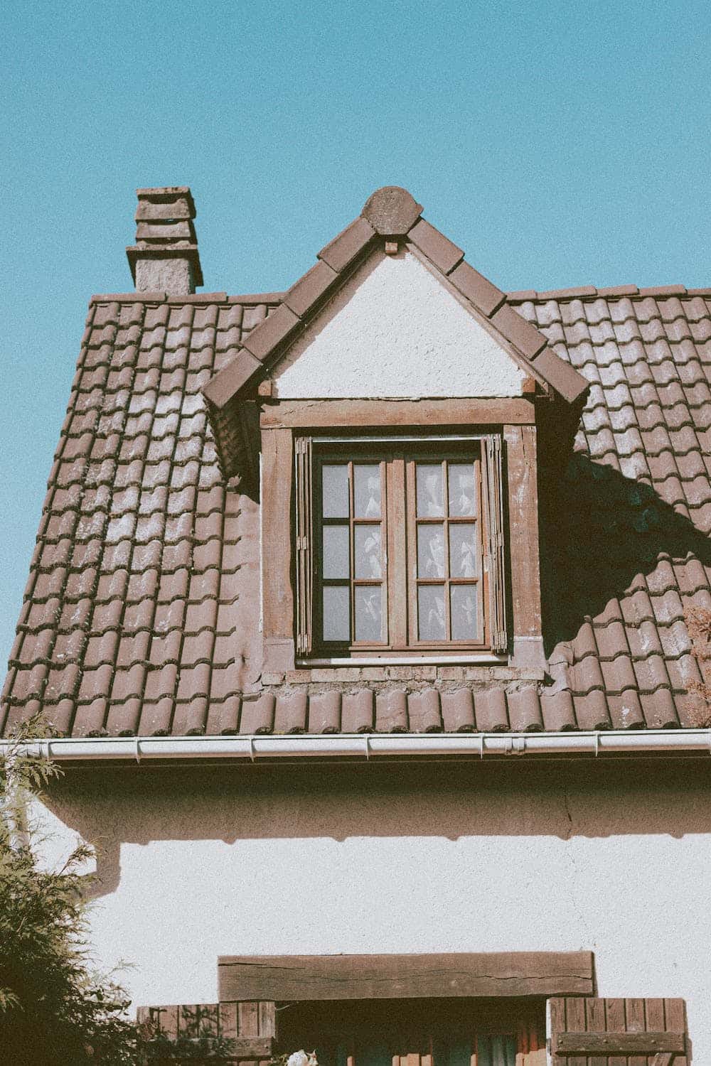 Vintage mangalore tile roof with wooden framed attic window and sloped clay tiles