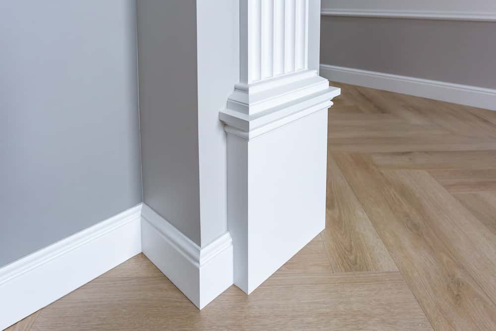 White baseboard wall moulding designs with detailed column corner finish on wooden floor