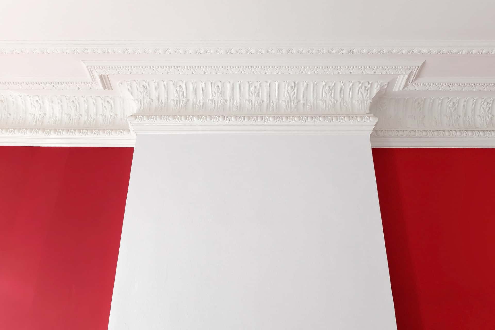 Intricate white crown wall moulding designs against bold red accent walls in a living space