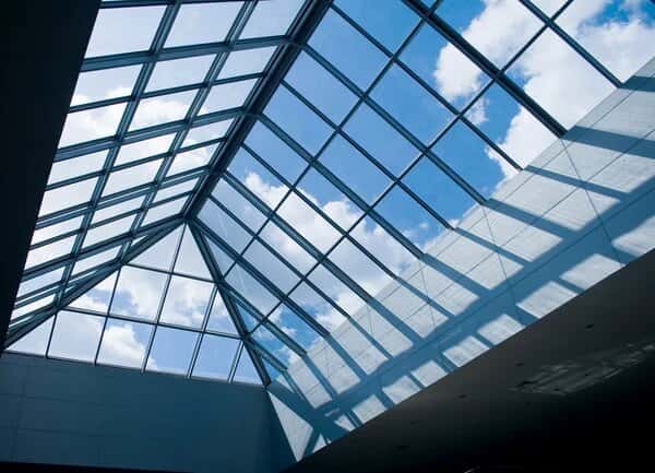 Modern glass ceiling design with sloped panels and clear blue sky view
