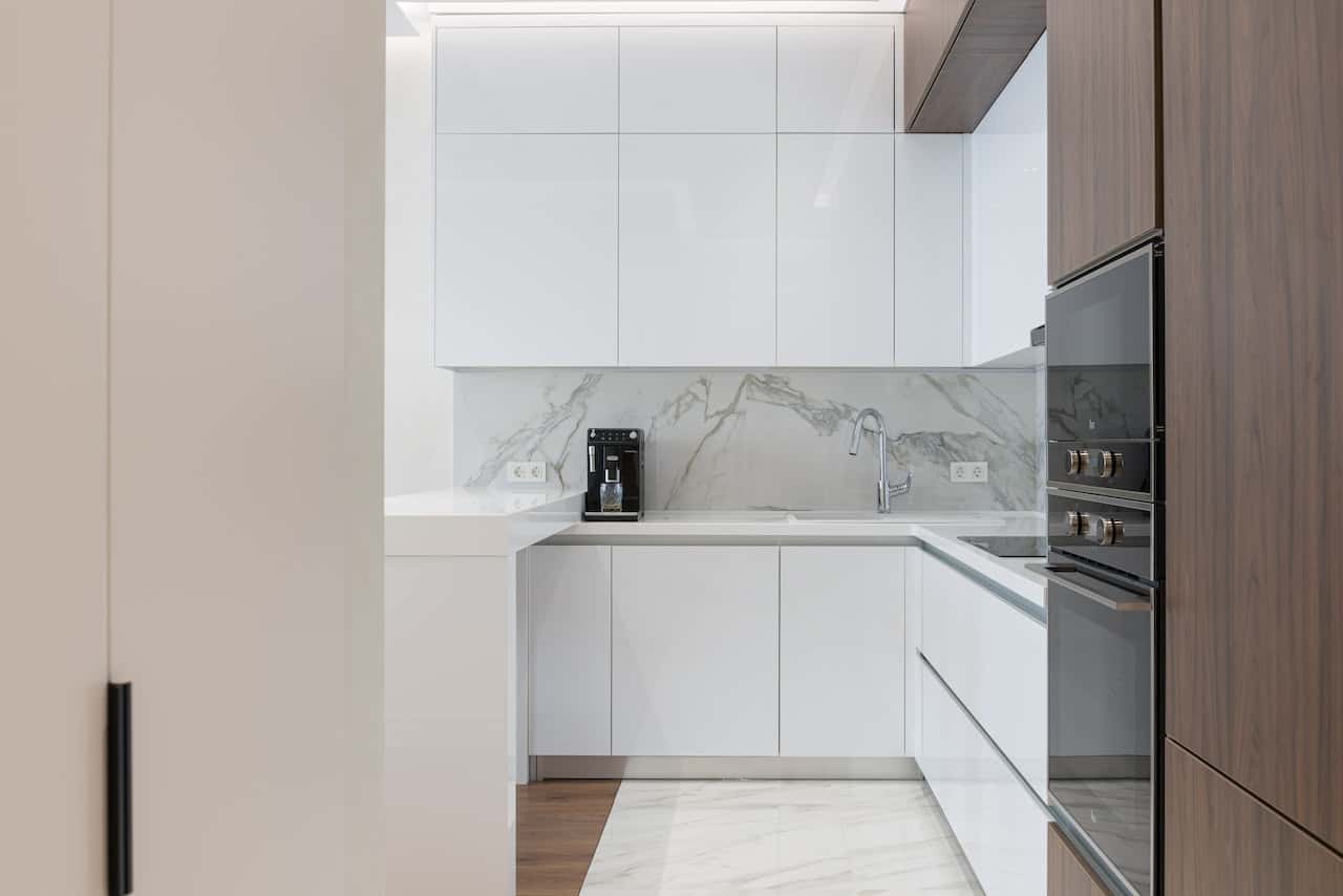 White gola profile handles in a compact marble kitchen with wood accents