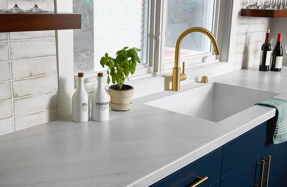 Stylish Kitchen Platform Designs white countertop, gold faucet, blue cabinets.