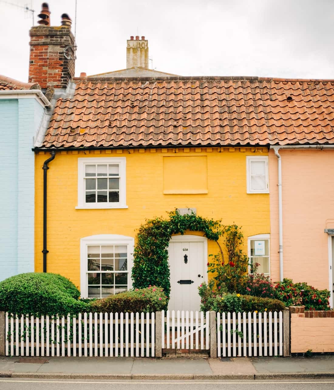 Charming mangalore tile roof cottage with yellow facade and white picket fence