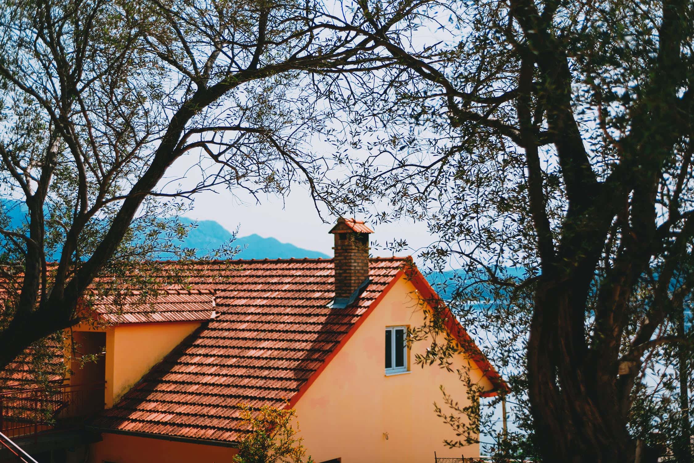 Scenic mangalore tile roof home with chimney, yellow walls and tree-framed view