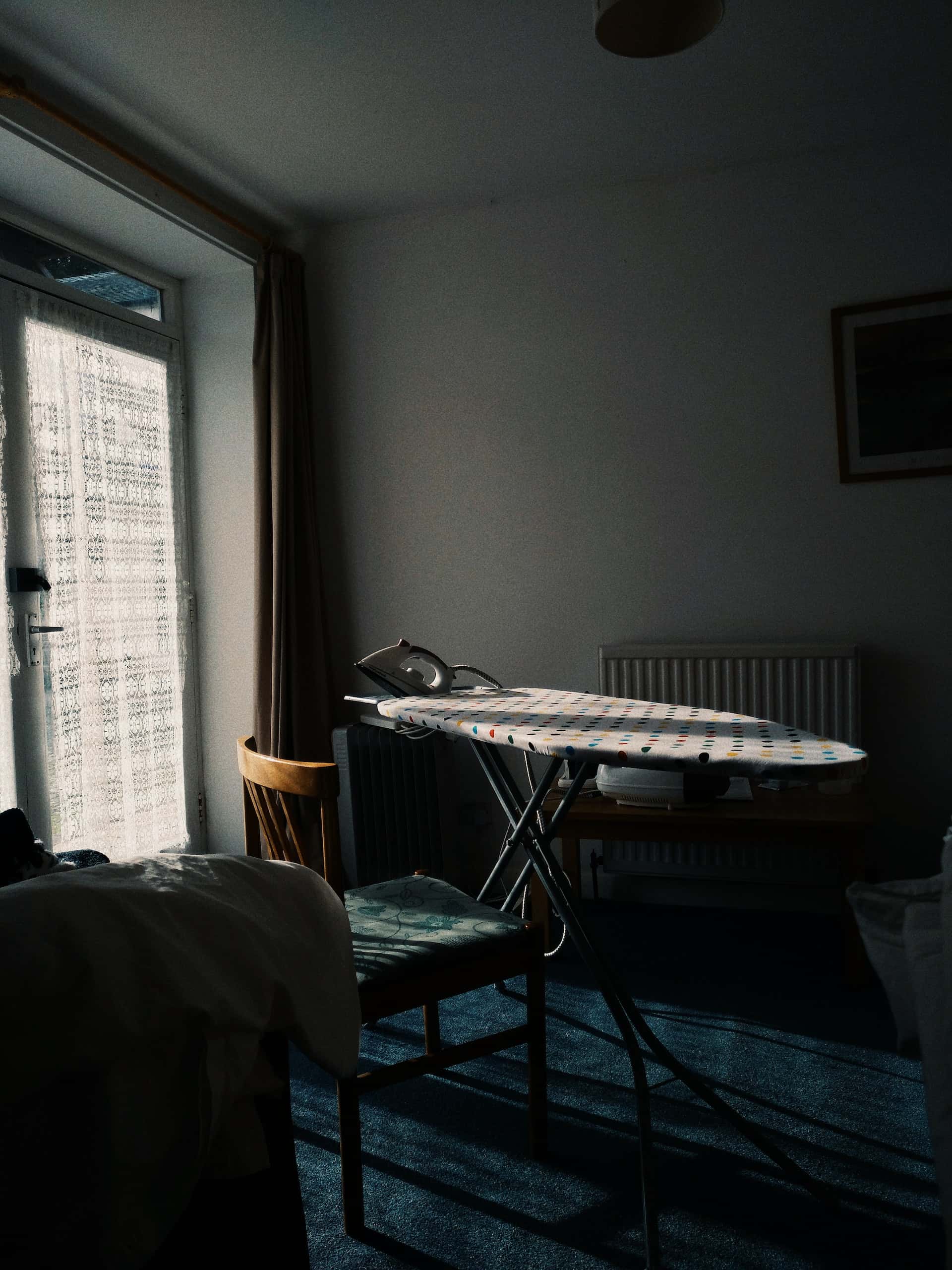 Ironing station near electrical points in bedroom with natural daylight and lace curtain