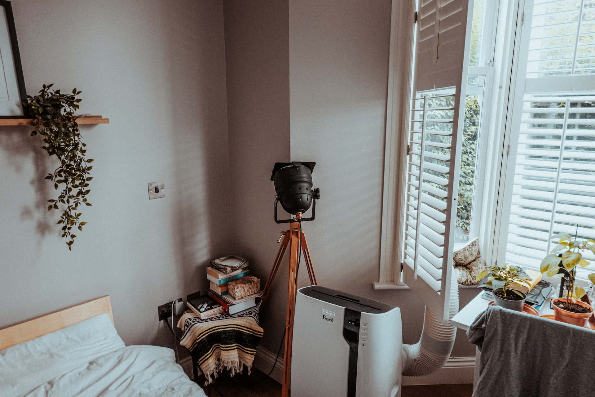Minimal bedroom corner design with tripod lamp, shelf plant, and portable AC