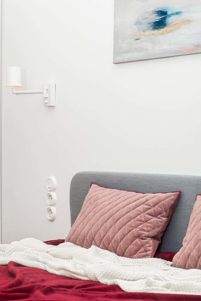 Minimal wall with electrical points in bedroom behind blush pink cushion pillows
