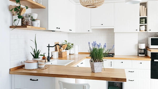 Bright modern kitchen cupboards in white with wood countertop and indoor plant accents