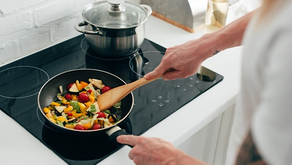 Cooking at the stove in a kitchen triangle layout with fresh vegetables in a pan