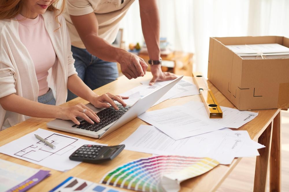 Couple planning home interiors on EMI with floor plans, color swatches, and paperwork