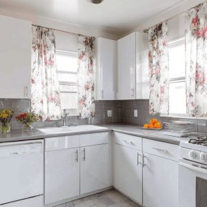Bright kitchen window curtain design with floral drapes enhancing airy white corner kitchen space