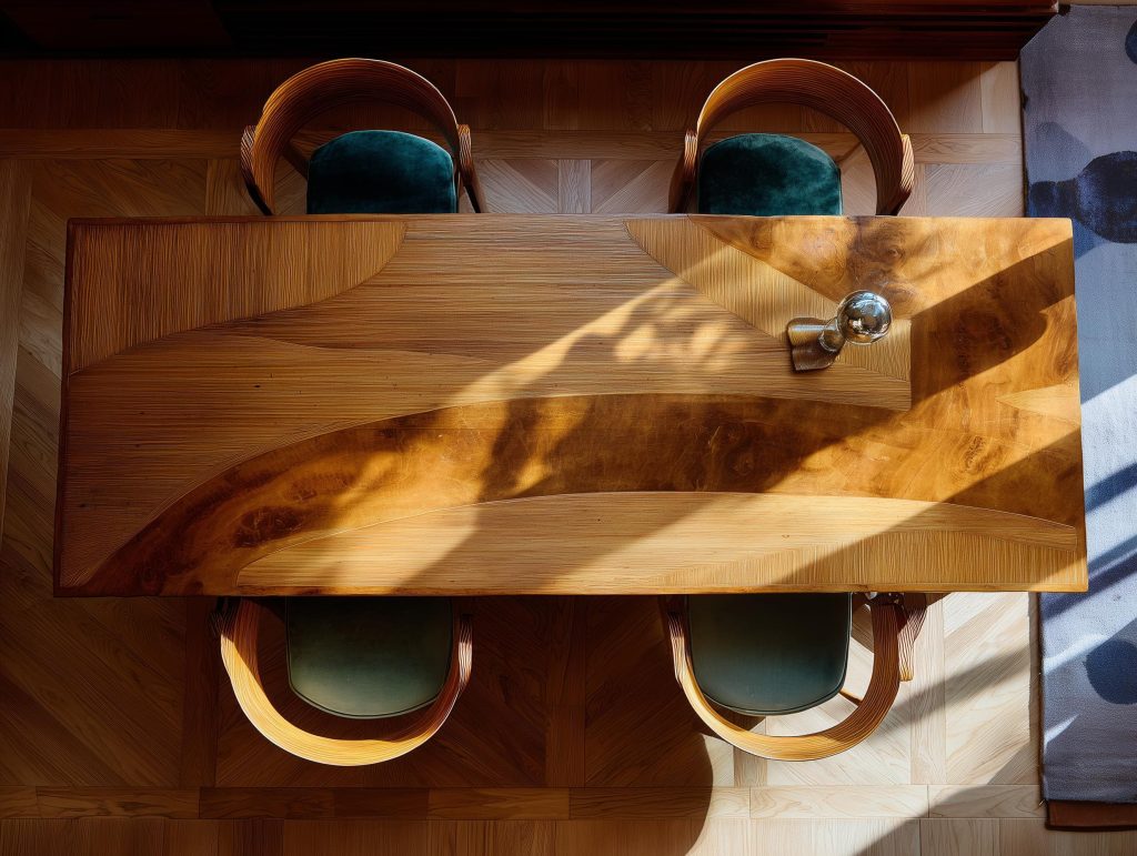 A premium wood dining table design featuring natural grain patterns and curved velvet chairs.