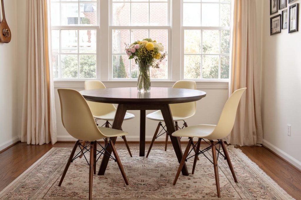 Modern glass tables for dining room layouts featuring a round dark wood base and cream Eames chairs.