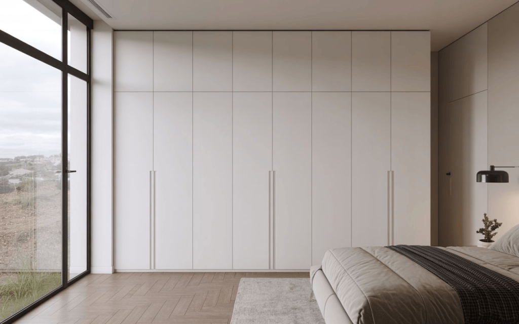 A minimalist floor-to-ceiling white duco paint wardrobe in a bright modern bedroom.