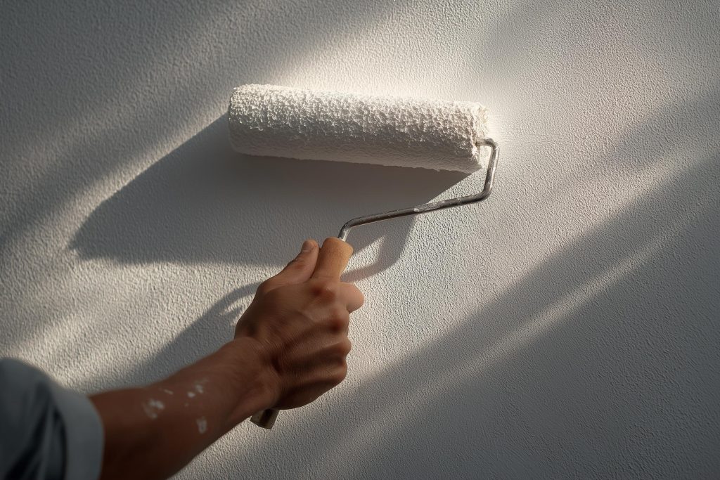  applying acrylic paint on walls with roller